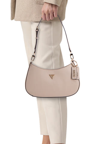 Sac à bandoulière beige de Guess, avec anse et pendentif Guess, porté par un mannequin dans un pantalon et une veste beiges.