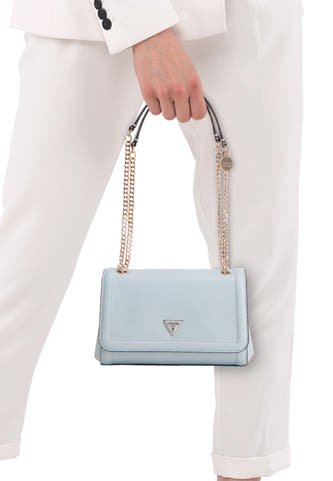 Sac à bandoulière bleu Guess, avec chaîne dorée et logo visible, porté par une personne en pantalon blanc et blazer.