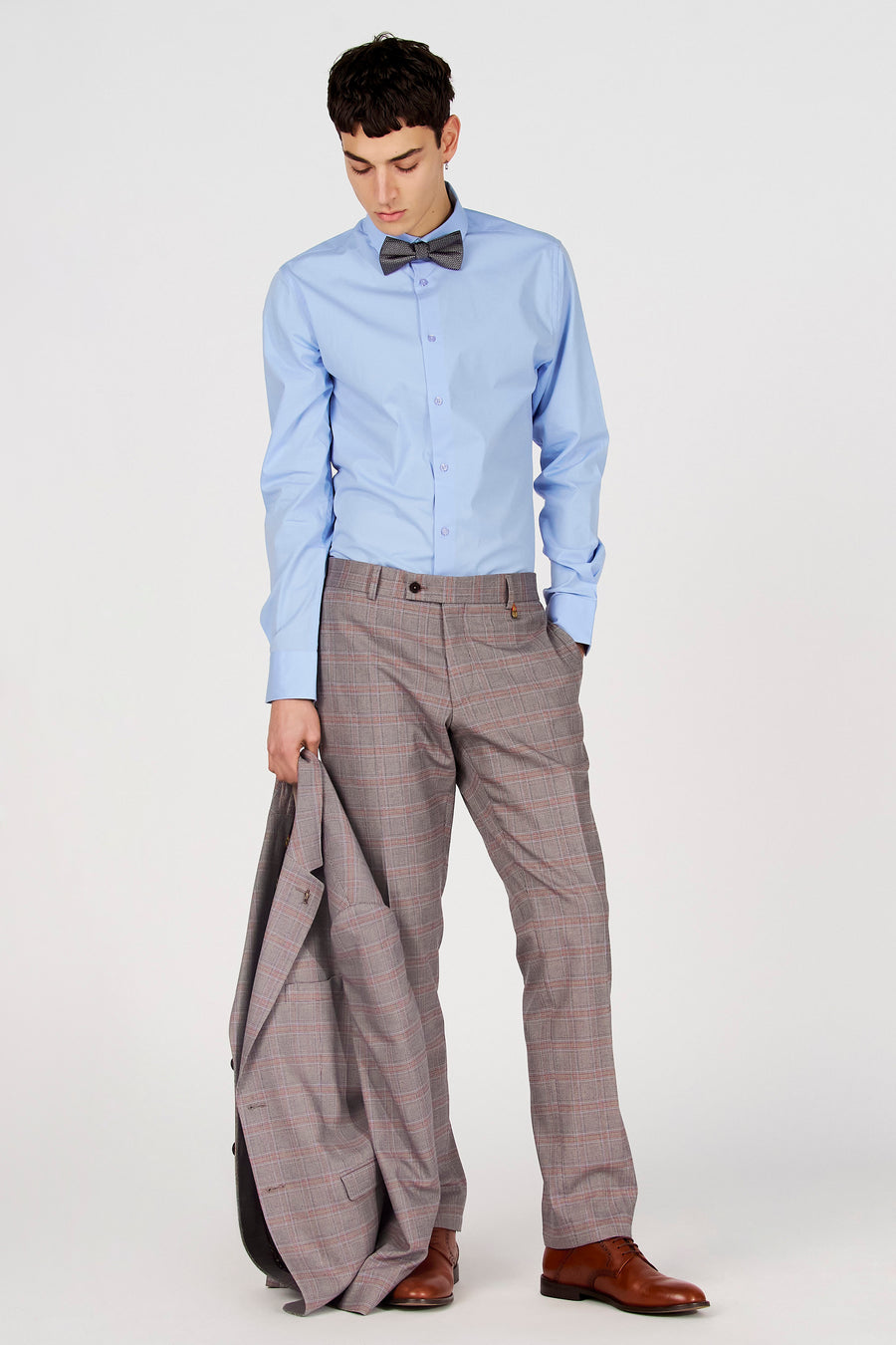 Chemise bleue à manches longues de Le Fabuleux Marcel de Bruxelles, portée avec un nœud papillon gris et un pantalon à carreaux.