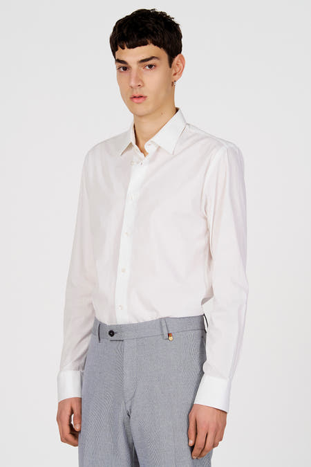 Chemise blanche à manches longues de Le Fabuleux Marcel de Bruxelles, portée avec un pantalon gris.