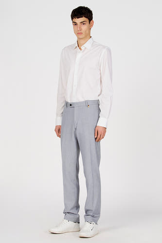 Chemise blanche à manches longues de Le Fabuleux Marcel de Bruxelles, portée avec un pantalon gris et des baskets blanches.