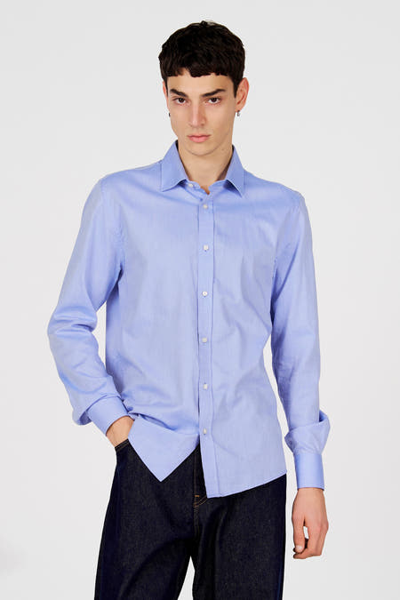 Chemise bleue à manches longues de Le Fabuleux Marcel de Bruxelles, avec fermeture boutonnée, portée avec un jean foncé.