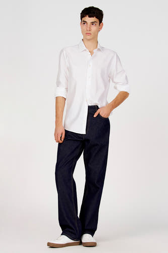 Chemise blanche à manches longues de Le Fabuleux Marcel de Bruxelles, portée avec un jean bleu foncé et des baskets blanches.