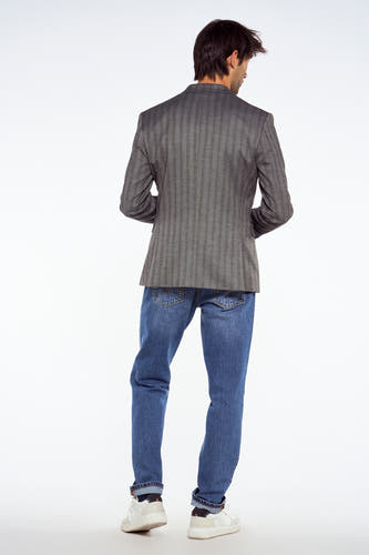 Blazer bleu de Le Fabuleux Marcel de Bruxelles, avec un motif à rayures, associé à des jeans et des baskets blanches, vu de dos.