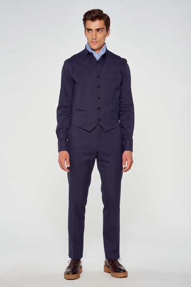 Een man in een marineblauw pak met een vest en bruine schoenen op een witte achtergrond.