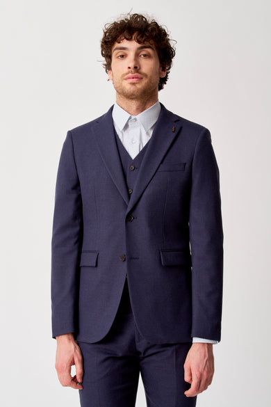 Blazer bleu de Le Fabuleux Marcel de Bruxelles, avec un gilet et une chemise à carreaux en dessous.