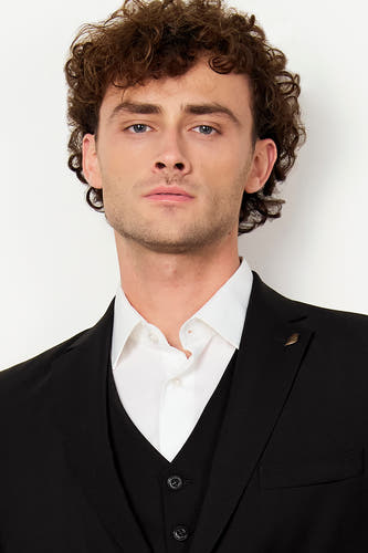 Zwarte blazer van Le Fabuleux Marcel de Bruxelles met een gouden reversspeld, gedragen over een wit overhemd en zwart gilet.