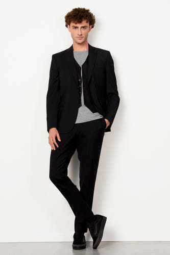 Blazer noir de Le Fabuleux Marcel de Bruxelles, avec une chemise et une cravate à carreaux de papillon, et un bouton doré.