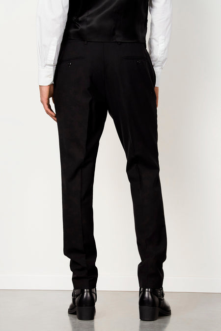 Pantalon de costume noir de Le Fabuleux Marcel de Bruxelles avec poches passepoilées, stylisé avec une chemise blanche, un gilet noir et des bottes noires, vue arrière.