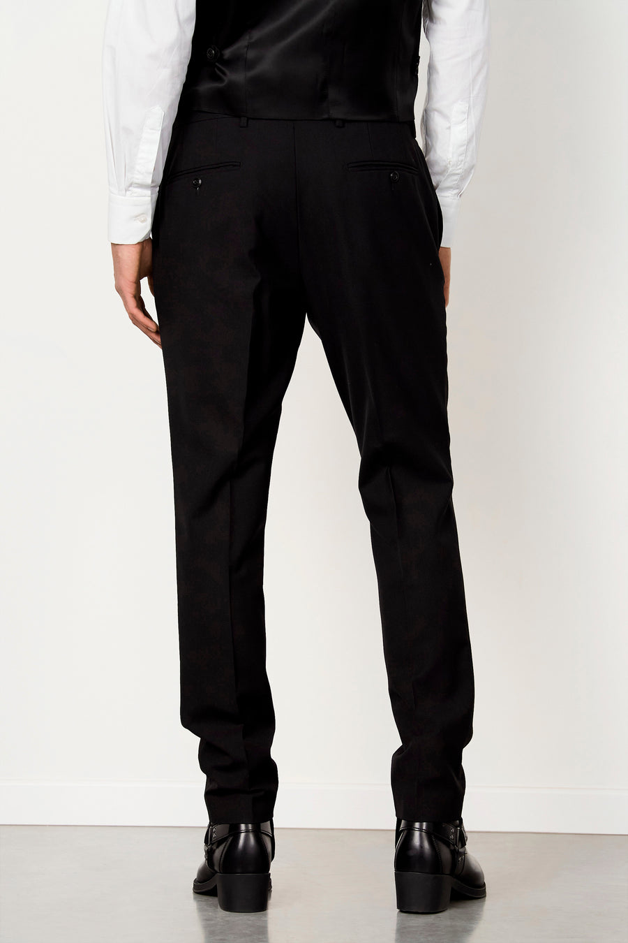 Pantalon de costume noir de Le Fabuleux Marcel de Bruxelles avec poches passepoilées, stylisé avec une chemise blanche, un gilet noir et des bottes noires, vue arrière.
