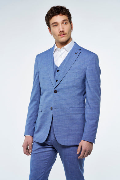 Blazer bleu de Le Fabuleux Marcel de Bruxelles, avec un motif de carreaux subtil, porté avec une veste et un chemisier blanc.