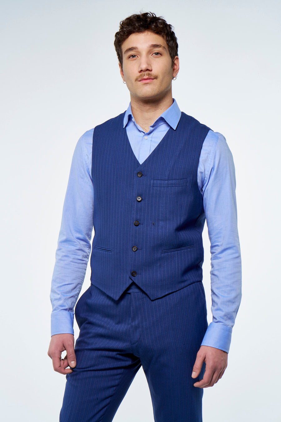 Gilet bleu à rayures craie de Le Fabuleux Marcel de Bruxelles, dos avec boucle réglable, porté sur une chemise bleu clair et un pantalon assorti.