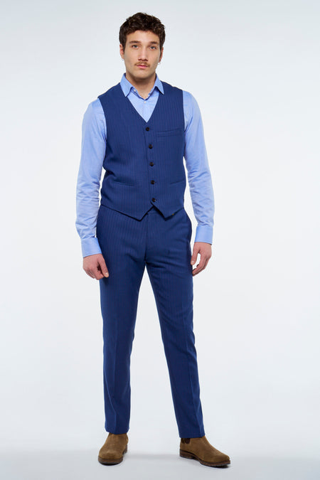 Gilet bleu de Le Fabuleux Marcel de Bruxelles avec fines rayures craie et boutons foncés, porté avec une chemise bleu clair, un pantalon assorti et des bottes en daim marron.