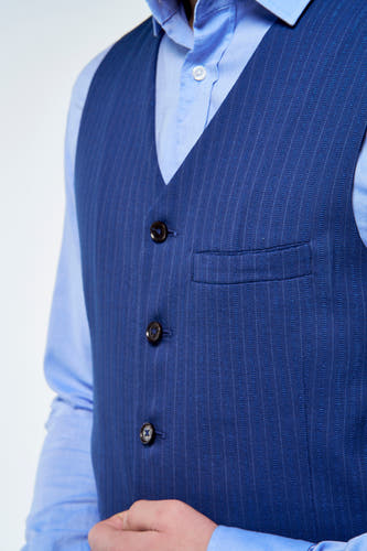 Gilet bleu de Le Fabuleux Marcel de Bruxelles avec fines rayures craie, trois boutons et poche poitrine à motif chevrons, sur chemise bleu clair.