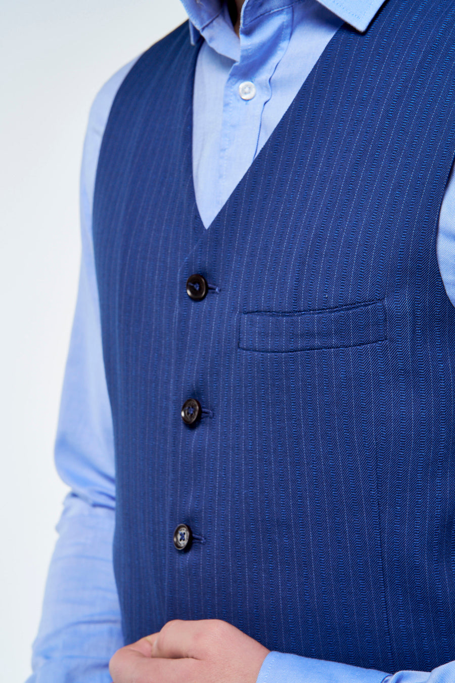 Gilet bleu de Le Fabuleux Marcel de Bruxelles avec fines rayures craie, trois boutons et poche poitrine à motif chevrons, sur chemise bleu clair.