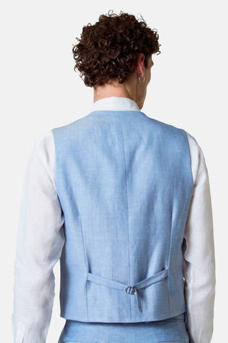 Gilet bleu de Le Fabuleux Marcel de Bruxelles, avec une ceinture ajustable et un chemisier blanc en dessous.