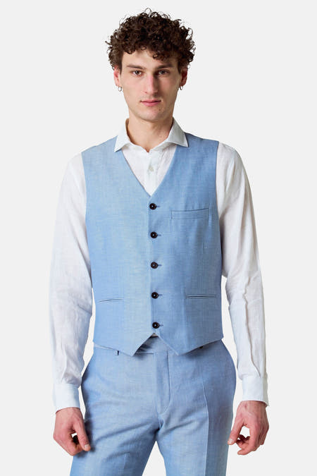 Gilet bleu de Le Fabuleux Marcel de Bruxelles, porté sur une chemise blanche et un pantalon coordonné.