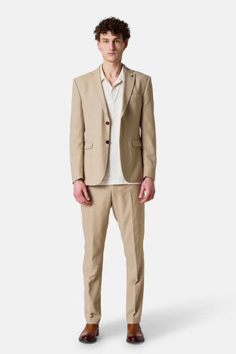 Blazer beige de Le Fabuleux Marcel de Bruxelles, porté sur un polo crème, avec une pantalon coordonné et des chaussures marrons.