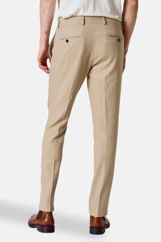 Pantalon de costume beige Le Fabuleux Marcel de Bruxelles, avec poches à boutons, porté avec des chaussures brunes.