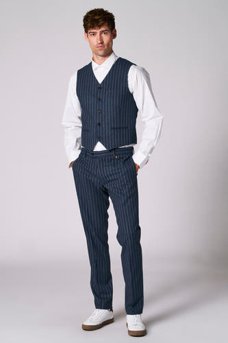 Gilet bleu de Le Fabuleux Marcel de Bruxelles, porté avec un chemisier blanc et un pantalon à rayures coordonnés.