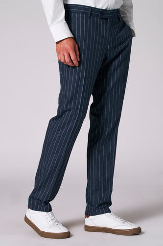 Pantalon de costume bleu avec une rayure blanche de Le Fabuleux Marcel de Bruxelles, porté avec un chemise blanc et des baskets blanches.