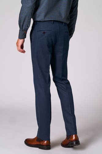 Pantalon de costume bleu Le Le Fabuleux Marcel de Bruxelles, vu vu de derrière, avec des chaussures marrons et une chemise à carreaux.