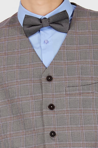 Gilet marron de Le Fabuleux Marcel de Bruxelles avec un motif à carreaux et des boutons marron, porté sur une chemise bleu clair avec un nœud papillon.