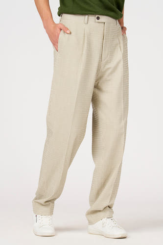 Pantalon de costume beige de Le Fabuleux Marcel de Bruxelles, avec rayures craie et plis, porté avec un haut vert et des baskets blanches.