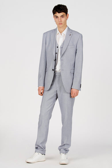 Blazer bleu de Le Fabuleux Marcel de Bruxelles, avec un gilet, une chemise et des baskets blanches.