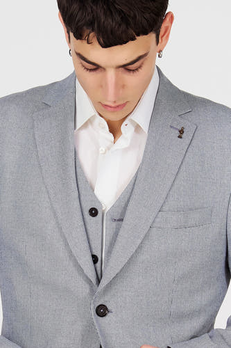 Blazer bleu de Le Fabuleux Marcel de Bruxelles, avec un motif subtil, une épingle de revers et porté sur une chemise blanche et un gilet.
