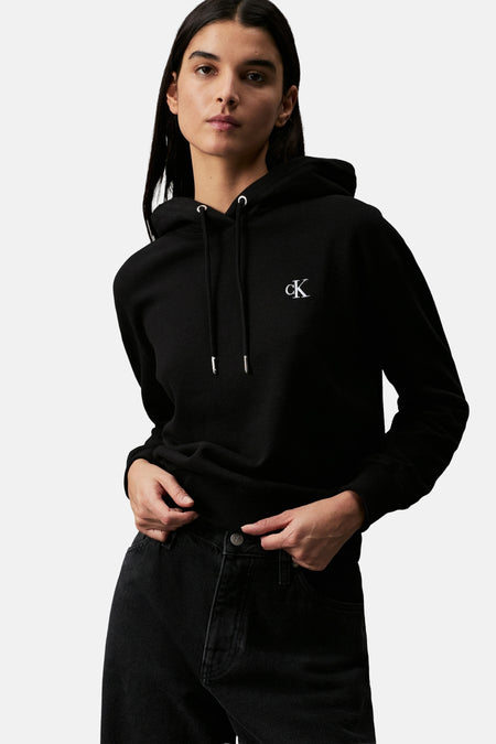 Pull-over noir de Calvin Klein, avec un petit logo sur la poitrine et porté avec un jean noir.