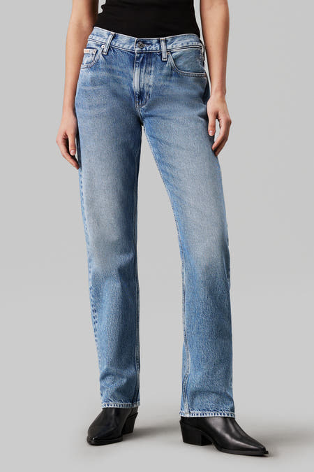Jean droit bleu clair de Calvin Klein, avec une légère usure et associé à des bottes noires.