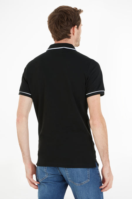 Polo noire Calvin Klein avec accents blancs sur le col et les manches, portée avec un jean bleu, vue de dos.
