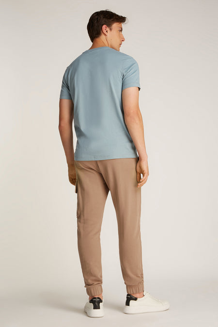 T-shirt bleu clair à manches courtes de Calvin Klein, d'une couleur unie et porté avec un pantalon marron et des baskets blanches.