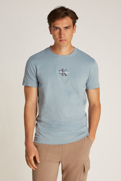 T-shirt bleu clair à manches courtes de Calvin Klein Jeans, avec un petit logo sur la poitrine et porté avec des shorts kaki.
