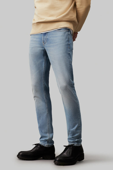 Jean tapered bleu clair de Calvin Klein, avec un logo 'CK' caractéristique sur la poche arrière.