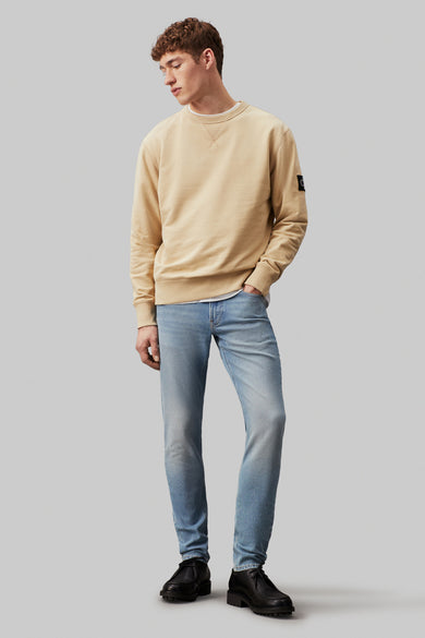 Lichtblauwe tapered jeans van Calvin Klein, gecombineerd met een beige sweater en zwarte schoenen.
