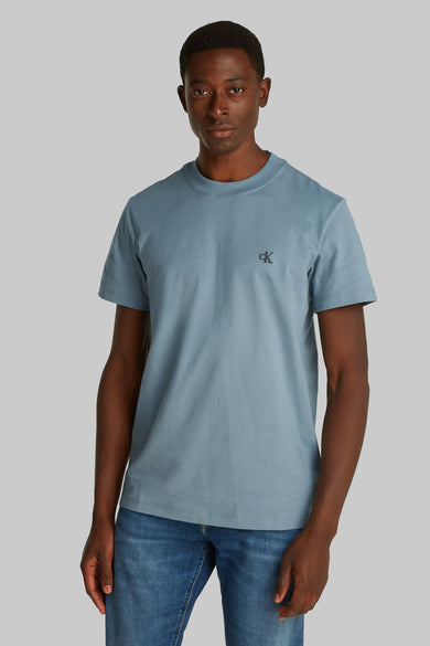 T-shirt bleu à manches courtes de Calvin Klein, avec un design simple, porté avec des jeans et des baskets blanches.