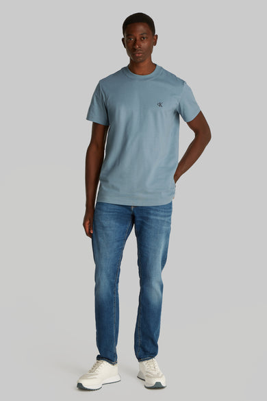 T-shirt bleu à manches courtes de Calvin Klein, porté avec des jeans et des baskets blanches.