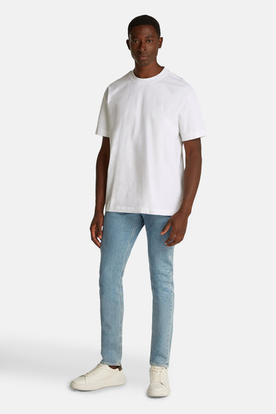 T-shirt blanc à manches courtes de Calvin Klein, avec un logo subtil sur la poitrine, associé à des jeans légers et des baskets blanches.