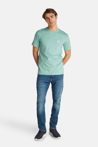 T-shirt turquoise à manches courtes de Calvin Klein, porté avec des jeans bleus et des baskets bleu marine.