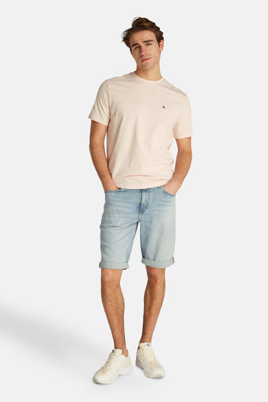 Jeansshort in lichtblauw denim van Calvin Klein, met omgeslagen pijpen en gedragen met een T-shirt en witte sneakers.
