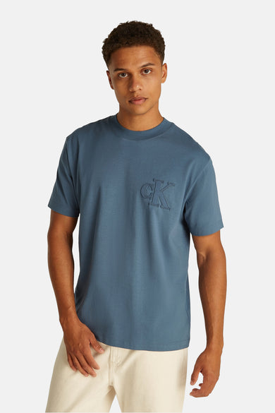 T-shirt bleu à manches courtes de Calvin Klein, d'une couleur unie et associé à des pantalons légers et des baskets blanches.