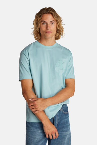 T-shirt turquoise à manches courtes de Calvin Klein, avec un logo subtil sur la poitrine et porté avec des jeans.