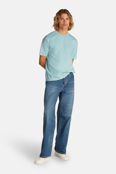 T-shirt turquoise à manches courtes de Calvin Klein, porté avec des jeans larges et des baskets blanches.