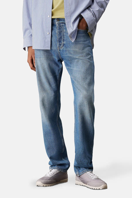 Jean droit mi-mollet bleu denim de Calvin Klein, avec un effet légèrement délavé et des baskets grises.