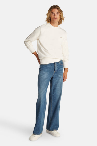 Gilet écru de Calvin Klein, avec des manches longues, associé à des jeans bleus et des baskets blanches.