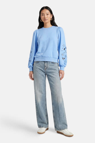 Blauwe sweater van HAILYS, met lange pofmouwen met uitgesneden bloemmotieven, gecombineerd met een wijde jeans en witte sneakers.
