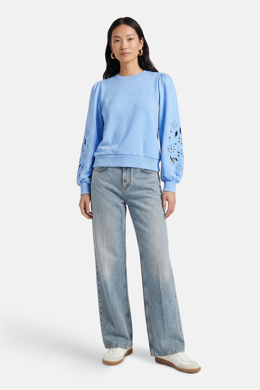 Blauwe sweater van HAILYS, met lange pofmouwen met uitgesneden bloemmotieven, gecombineerd met een wijde jeans en witte sneakers.
