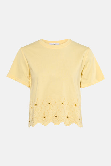 T-shirt jaune à manches courtes de HAILYS, fini avec broderie le long de l'ourlet, combiné avec un jean bleu foncé et des talons nude.
